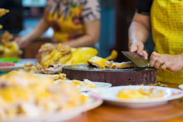 Focus on Asian chefs chopping boiled chicken on wooden chopping boards with large knife and serving on plates. Yummy and delicious food in Asia
