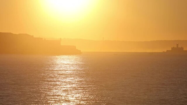 Lisbon. Portugal. A prominent landmark of the Forte do Bugio lighthouse set offshore. Drone footage of picturesque coast under sunrise sky with water reflections. High quality footage.