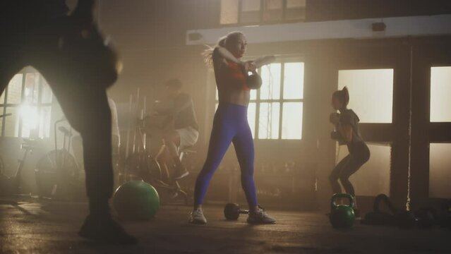 A group of five people doing fitness exercise at gym. Two men doing cycling exercise, man and woman lifting kettlebell, one woman lifting dumbbells