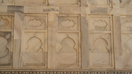 Details of the architecture of the ancient Taj Mahal. There are symmetrical decorative carvings and ornaments on the marble wall. India. Agra. Close-up