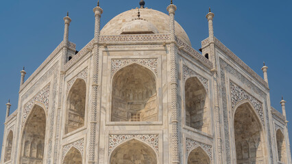 Fototapeta na wymiar The ancient white marble Taj Mahal against the blue sky. Symmetrical arches, domes and spires are visible. On the walls of the mausoleum there are ornaments and inlays of precious stones. India. Agra 