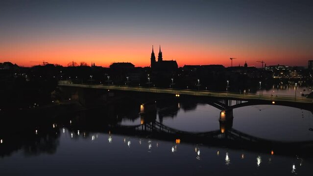 Drone dolley shot of the Wettstein bridge with the silhouettes of the Munster Cathedral in the skyline of the city Basel during after sunset.