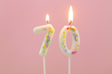 White decorated burning birthday candles on pink background, number 70