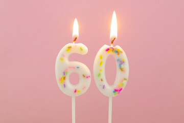 White decorated burning birthday candles on pink background, number 60