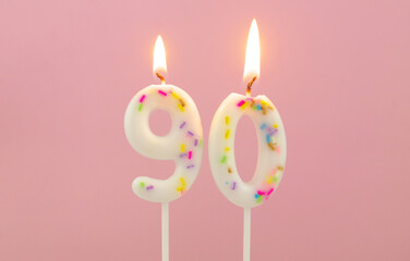 White decorated burning birthday candles on pink background, number 90