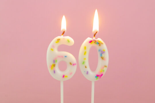 White decorated burning birthday candles on pink background, number 60