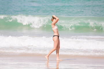 A young woman listening to music with her earphones is walking along the shore