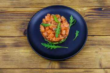 Salmon tartare with avocado and arugula on wooden table. Top view