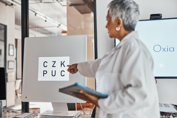 Naklejka premium Letter eye exam, chart and senior woman doctor pointing to eyes test and clinic assessment sign. Consulting, optometrist and tablet of a healthcare employee in a office for wellness and health