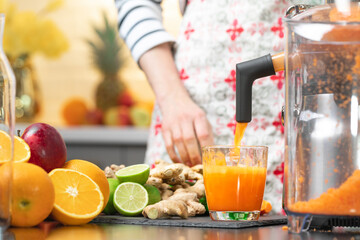 Squeezing carrot juice with juicer healthy citrus fruits in background. Intake vitamins detox,...
