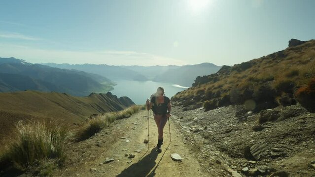 Fit active woman walking up steep mountain path towards Isthmus Peak, bright sunshine