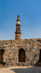 The ancient temple complex of Qutub Minar. Weathered sandstone brick walls with arches. The world's tallest minaret against the blue sky. India. Delhi.