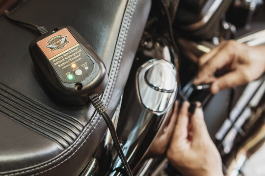 BANGKOK,THAILAND - February 22-2023: Battery Charger Maintainer Trickle for Harley Davidson Motorcycle on seat with hand connect the tender plug to motorcycle background at garage.