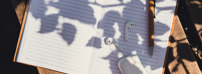 Paper notebook with wireless headphones. Mockup Coffee break. Audio healing, sound therapy wellness rituals, positive mental health habits listening podcast writing self discovery gratitude journal
