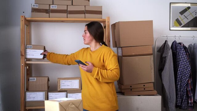 Female small business owner using mobile app on smartphone checking parcel box. Online shop seller scanning retail dropshipping package postal parcel bar code on cell technology.