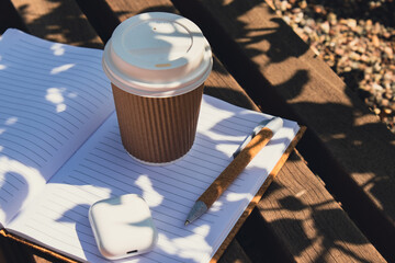 Take away coffee in craft recycling paper cup with paper notebook with wireless headphones. Mockup Coffee break. Audio healing, sound therapy wellness rituals, positive mental health habits listening