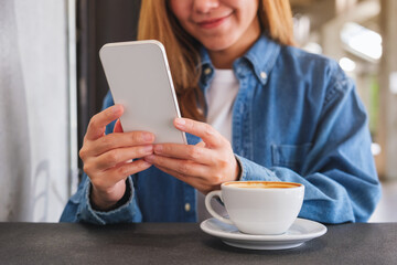 Closeup image of a young woman holding and using mobile phone in cafe