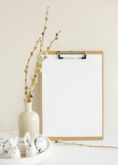 Easter background. Wooden clipboard with blank paper and copy space,spring willow branches in a vase and Easter eggs and funny bunny in neutral colors.
