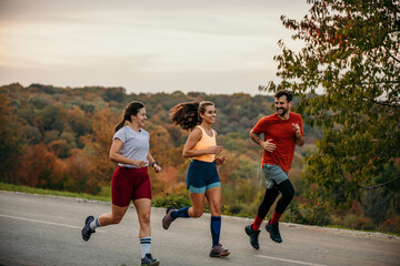 A small group of fit athletes enjoying running and communicating while jogging in nature.