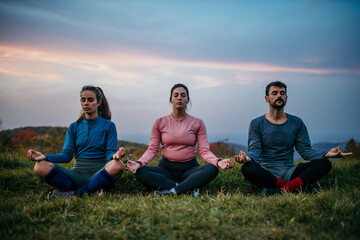 Three people meditating outdoors. Two people observed a guided meditation from a female yoga instructor