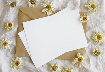 Greeting card mockup and dry daisy flowers pattern on beige linen texture background top view flatlay. Card mockup with copy space.