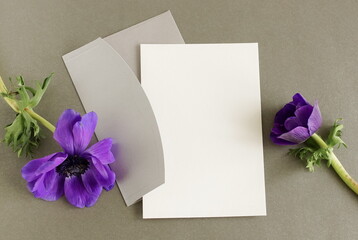 Greeting card mockup, envelope and purple flower anemone on dark gray background top view flatlay. Card mockup with copy space.