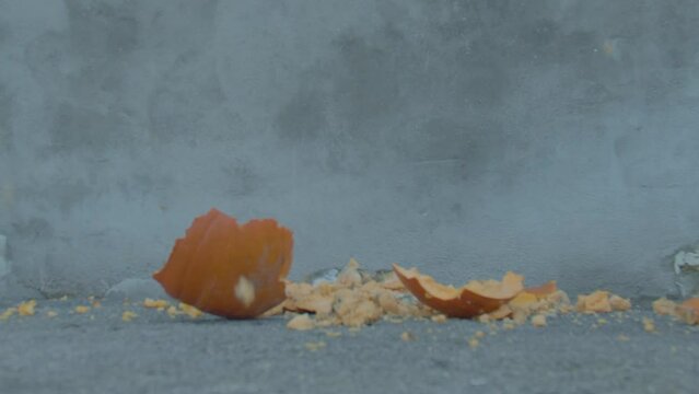 Halloween pumpkin is smashed into pieces in slow motion after being dropped onto ground.