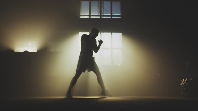 Full shot of a young athlete doing shadow boxing by himself in slow-motion. Performing series of powerful jabs, punches and uppercuts
