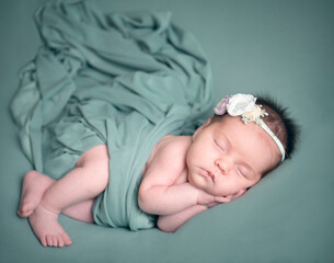 Cuddly sleeping newborn infant girl wrapped in green with flower headband - 574160151