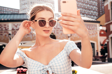 Young beautiful smiling hipster woman in trendy summer dress clothes. Sexy carefree model posing on the street background at sunset. Positive blond female outdoors. Cheerful and happy. taking selfie