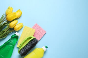 Spring cleaning. Detergents, flowers, brush and rags on light blue background, flat lay. Space for...