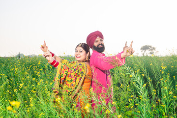 Happy Punjabi sikh couple doing bhangra dance in agriculture field celebrating Baisakhi or vaisakhi...