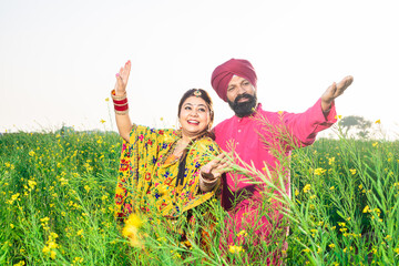Cheerful Punjabi sikh couple doing bhangra dance in agriculture field celebrating Baisakhi or vaisakhi festival.