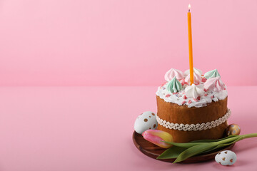 Traditional Easter cake with meringues, candle, decorated eggs and tulip on pink background. Space for text