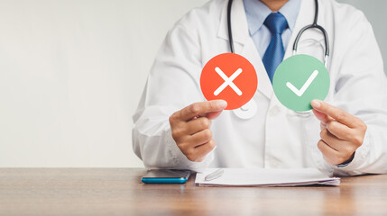 Doctor holding red and green papers with a checkmark and a cross while sitting at the table in the...