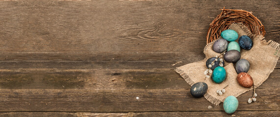 Easter eggs in wicker basket and blooming cherry on old wooden background. Festive greeting card