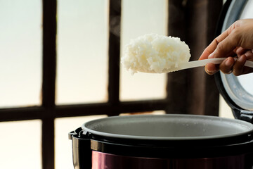 White rice is spooned with steam from an electric rice cooker. hot food concept