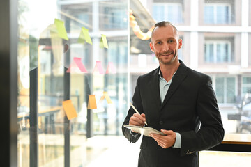 Portrait of confident caucasian businessman in suit holding digital tablet and smiling at camera