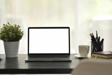 Black wooden desk with laptop computer, potted plant and stationery. Blank screen for your advertisement