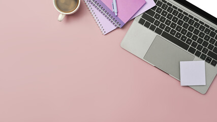 Top view of laptop computer, sticky notes, notebooks and coffee cup on pink background