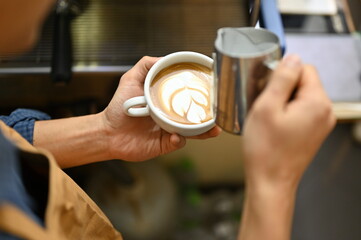 Fototapeta na wymiar Close-up image, An Asian male barista holding a beautiful latte cup, making beautiful latte art