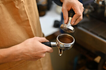 Fototapeta na wymiar Professional male barista holding portafiler, using coffee tamper to press coffee powder