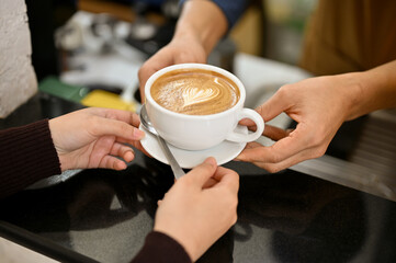 a male barista handing a cup of latte to a customer in the coffee shop.