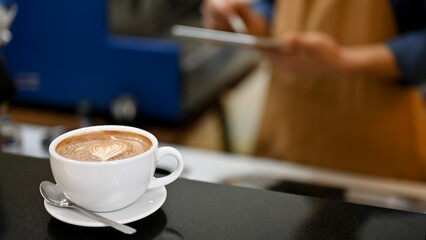 Beautiful latte or cappuccino coffee cup is on a black countertop in the coffee shop.