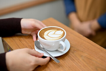 Close-up image of a female customer's hands holding a cup of latte, sipping coffee