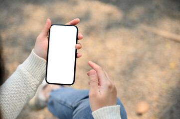 Obraz na płótnie Canvas a woman's hand holding a smartphone white screen mockup over blurred street in background.