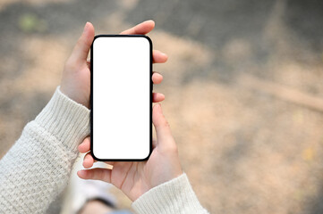 A woman holding a smartphone white screen mockup over blurred street in background. - obrazy, fototapety, plakaty