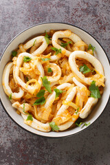 Spanish cuisine stewed calamari with onions in white wine close-up in a bowl on the table. Vertical top view from above