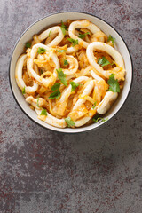 Squid with caramelized onions Calamares encebollados closeup on the plate on the table. Vertical top view from above