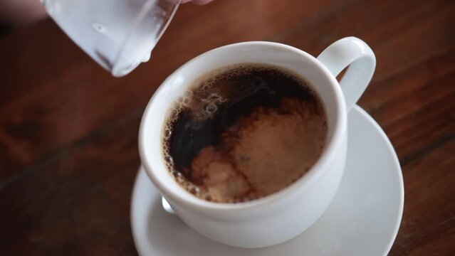 Adding milk to a cup of black coffee. White and brown swirling. Slow motion.